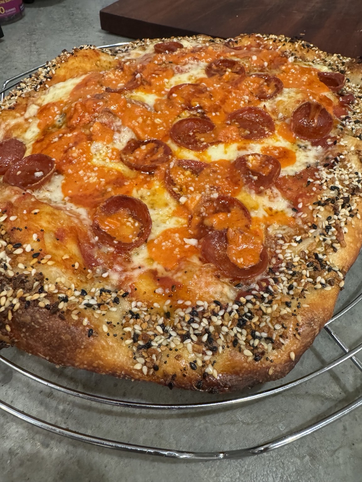 Greg’s finished pepperoni pizza with a browned, seeded crust on a cooling rack.